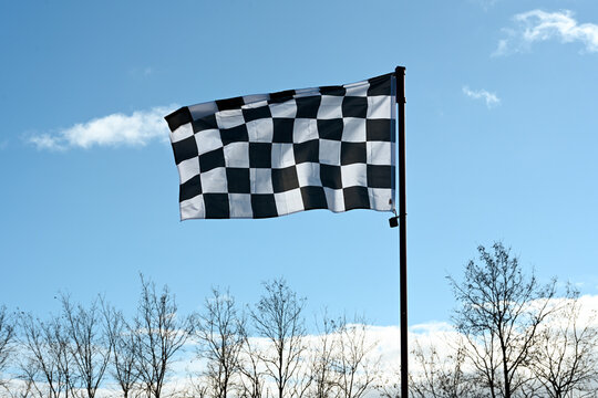 Drapeau &agrave; damier flottant sur fond de ciel bleu, au-dessus de la cime des arbres