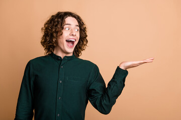 Photo of cheerful positive attractive funny man wear green stylish clothes hold look banner empty space isolated on beige color background