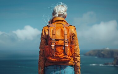 A woman wearing a brown jacket and orange backpack stands on a cliff overlooking the ocean. Concept of adventure and exploration, as the woman is ready to embark on a journey or hike - Powered by Adobe