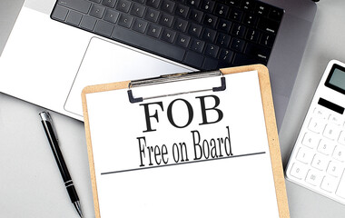 FOB- FREE ON BOARD word on clipboard on laptop with calculator and pen