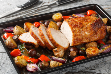 Delicious festive baked pork loin with vegetables and mushrooms close-up on a baking sheet on the...