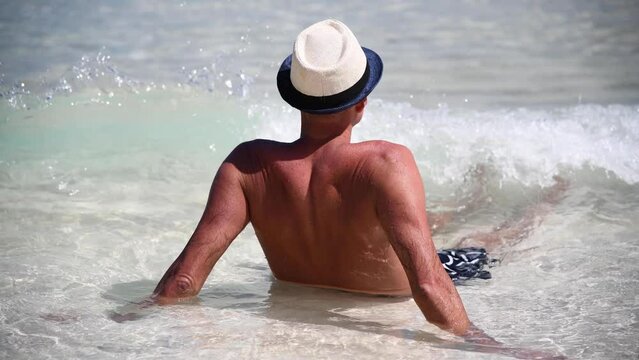 Man wearing straw hat enjoying crystal clear waters ocean, slow motion
