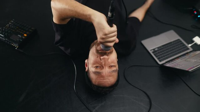 Recording session: Rapper or singer male reclines, using gestures to convey emotions while recording new music