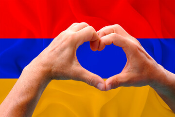 close-up of male hands in heart form against background of silk national flag of Armenia, patriots...