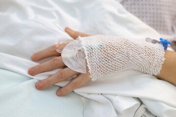 A woman's hand with a bandage and an intravenous line, in a hospital bed.