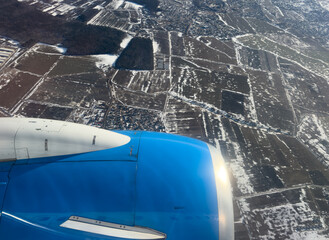 Jet engine and wing seen through airplane window during flight over landscape. Airplane engine