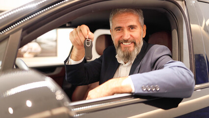 Happy mature man sitting in the brand new car at the salon and holding the car keys