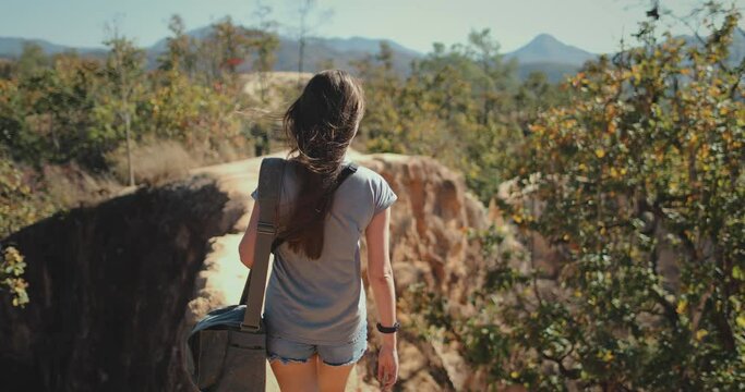 A woman wearing a backpack is trekking up a hill in Thailand, captured in slow motion.