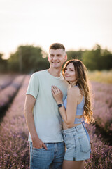 Beautiful woman hugs man among violet flowers with sunlight on summer day. Romantic young couple having fun together in purple lavender field. Female embracing male enjoying romantic time in sunset.