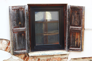 Rustic style aged window with shutters at rural home wall painted white with visible red bricks