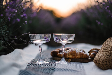 Two glasses of white wine with lavender sprigs on background of lavender field. Straw basket and...