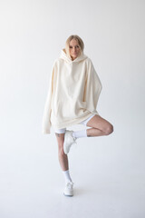 Beautiful blonde woman posing in white hoodie and leggings posing against white background