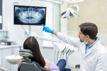 Professional male dentist showing x-ray footage of teeth to female patient in clinic office