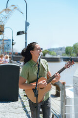vertical image of young long haired busker man playing guitar and singing in Puerto Madero Argentina