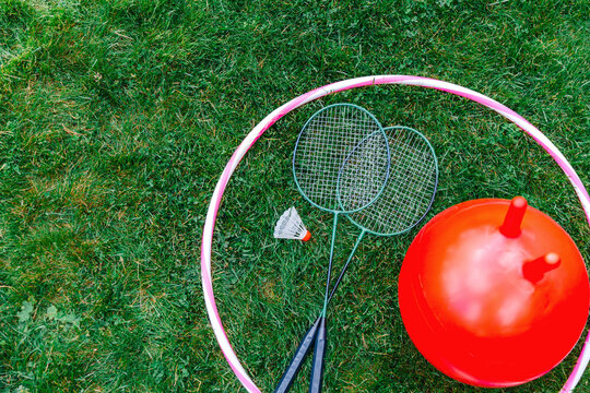 leisure games, sport equipment and toys concept - bouncing ball or hopper, hula hoop and set of badminton rackets with shuttlecock on grass