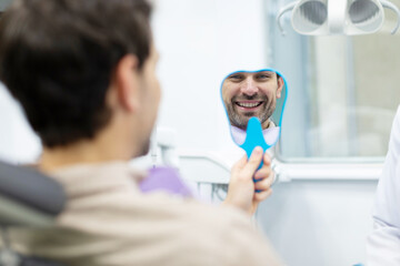 Rear view of man patient of dental clinic looking at mirror, happy with his beautiful smile