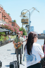 vertical image of young long haired busker man playing guitar and singing in Puerto Madero Argentina