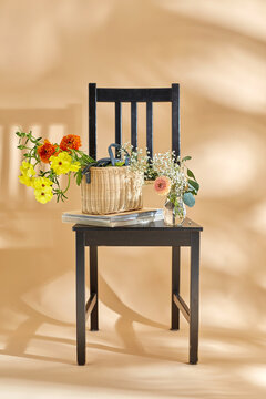 home decor and design concept - close up of flowers in basket and magazines on vintage chair over beige background