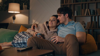 Loving family watching television together sitting cozy couch late evening.