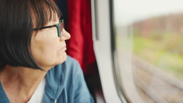 Close up of old woman looking out the train window while traveling, soft focus. Pensive elderly lady riding on the train looking out the window, Slow motion 