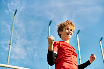 A young boy in a vibrant red shirt stands confidently holding a baseball bat, ready to swing. His focused expression and strong grip indicate his passion for the sport.