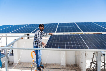 Indian worker installing solar panels on roof of house. Maintenance of photovoltaic panel system....