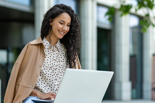 Portrait of a smiling young professional woman using a laptop in an urban outdoor setting, exuding confidence and positivity.