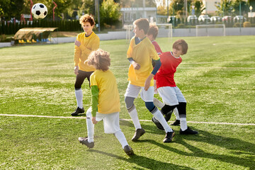 A group of young children dressed in colorful jerseys, they dribble the ball, pass, and shoot towards the goal, showcasing their teamwork and skills on the field.