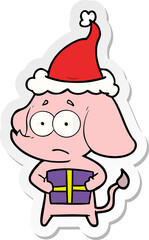 hand drawn sticker cartoon of a unsure elephant with christmas present wearing santa hat
