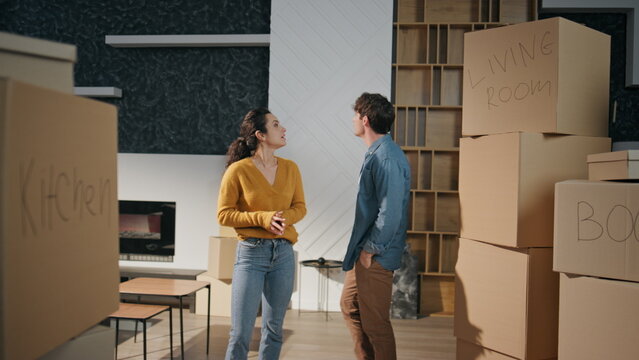 Happy couple moving house standing living room with boxes. Spouses enjoying home