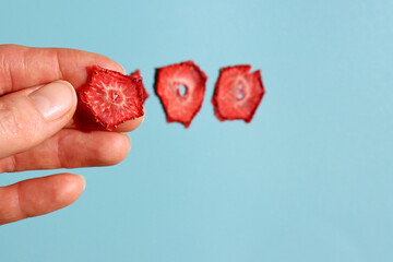 A thin slice of dried strawberry in a woman's hand on a blue background.