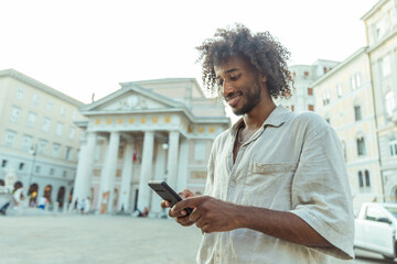 A man with curly hair is looking at his cell phone in a city square
