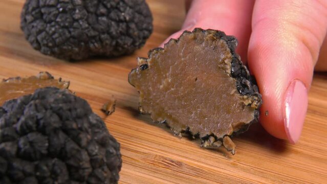 A knife cuts a slice from a black truffle on a wooden board. Close-up. High quality 4k footage