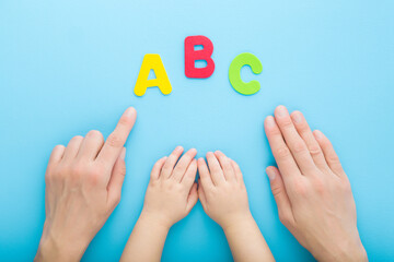 Young mother finger showing colorful abc letters to baby. Hands together on light blue table background. Pastel color. Time to learning. Point of view shot. Closeup. Top down view.