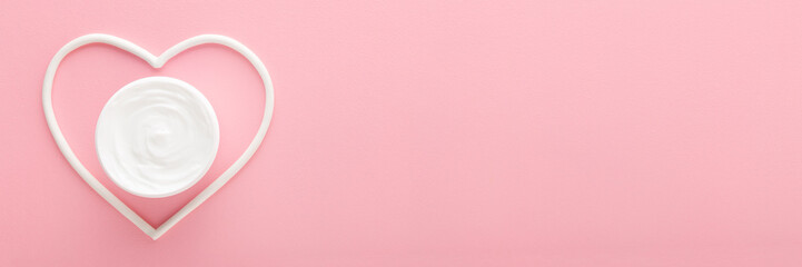 White heart shape with cream jar on light pink table background. Pastel color. Care about female...