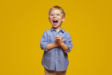 Little surprised child wearing striped blue shirt and stylish glasses clapping hands and yelling in...