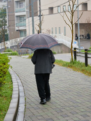 雨の日の住宅地で歩く一人のシニア女性の姿