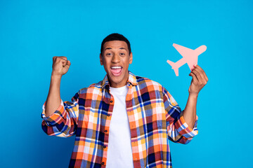 Photo of nice young man hold small plane raise fist wear shirt isolated on blue color background