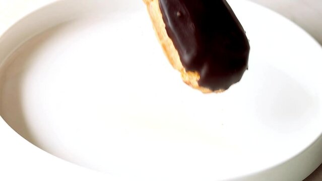 Eclairs. Hand taking eclair from white plate. Close up of woman's hand with eclair. Woman's hand picking eclair with chocolate icing from white plate, glazed dessert close-up