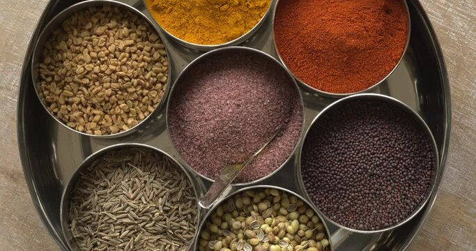 Top view of spices box or Indian masala dabba with seven containers and a little spoon on a rustic wooden table. 