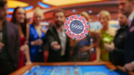 Casino Enthusiasts Making Calculated Bets at a Roulette Table. International Crowd of Young Beautiful and Handsome Adults Enjoying the Night Out Activity. Gambler Tossing a Chip In Front of a Camera