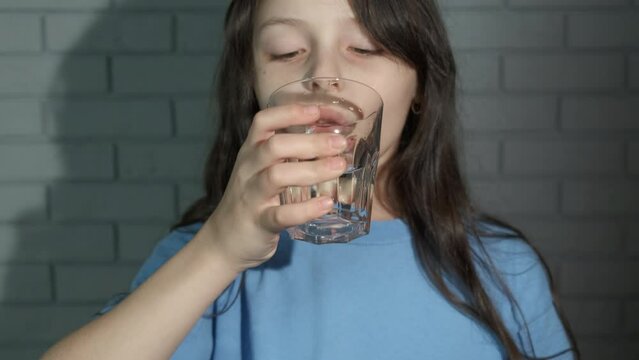 Child show filtered water in glass. A view of little girl drink water from glass by the wall. A concept of using filtered and pure water ay home.