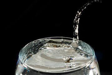 Close-up of a transparent glass cup with water inside and drops making a splash.