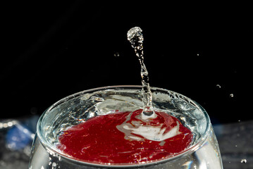 Transparent glass bowl, filled with water, with red reflection and splashing drops. Splash Effect.