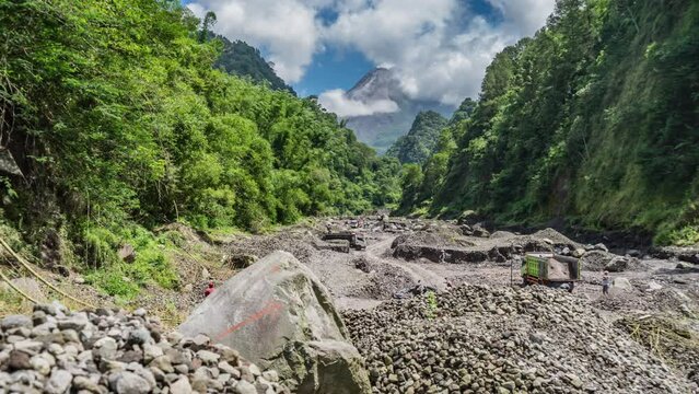 Yogyakarta, Indonesia - February 11, 2024. Morning activity of sand mining in the Boyong River with Merapi Mount in the background. Miners load the sand into trucks, then it is delivered to the buyer.