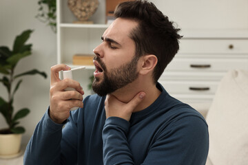 Young man using throat spray at home