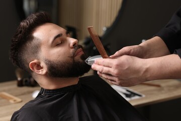 Professional barber trimming client's mustache in barbershop, closeup