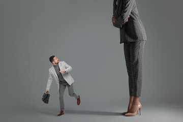 Small man running from giant woman on grey background