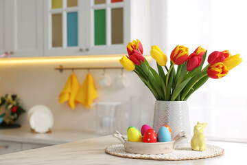 Easter decorations. Bouquet of tulips, painted eggs and bunny figure on table indoors. Space for...
