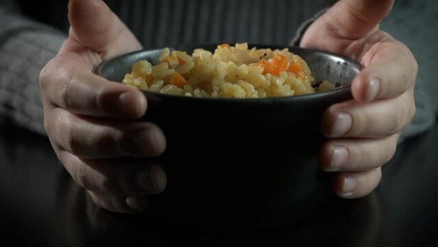 Refugee woman with rice bowl. A view of refugee female hands with bowl of rice against black background.